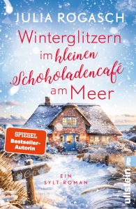 Cover von Winterglitzern im kleinen Schokoladencafé am Meer von Julia Rogasch: Verschneites Reetdachhaus an der Küste mit warm leuchtenden Fenstern, Schneeflocken im Vordergrund und blauem Himmel.